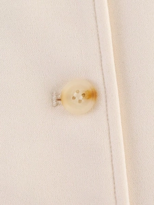 Close-up detail of textured cream fabric and amber resin button on women's jacket