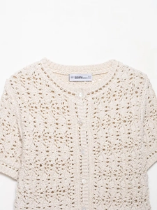 Détail de la texture au crochet et fermeture à boutons perlés du cardigan blanc en maille