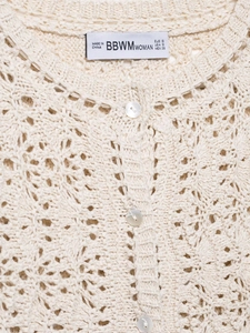 Détail du haut en crochet blanc cassé avec motifs floraux délicats et boutons perlés