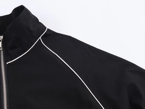 Close-up of black nylon jacket with high collar, silver zipper and white piping details
