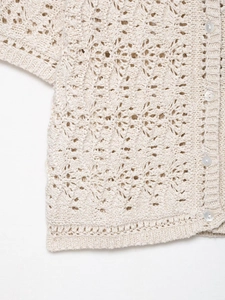 Détail d'un cardigan en maille crochet beige avec motifs ajourés et boutons nacrés élégants