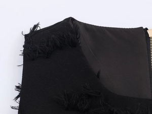 Detailed close-up of black woven fabric texture with fringe trim and gold metal zipper