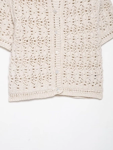 Vue détaillée de la texture crochetée beige et des boutons nacrés du cardigan