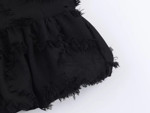 Detailed macro shot of the black textured frayed fringe fabric on the skirt's hemline