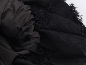Detail view of black textured fabric with spliced fringe edges and fringe hem design