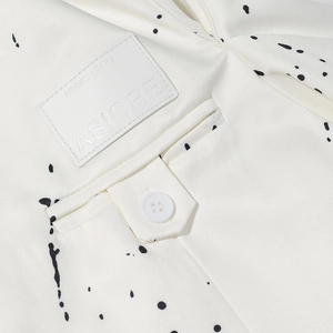 Macro shot of off-white blazer fabric with ink splatters, leather patch and button detail