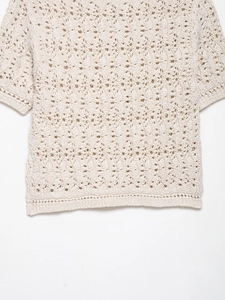 Détail d'un haut en crochet beige montrant des motifs ajourés délicats et un ourlet ondulé