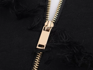 Close-up of black twill fabric featuring a gold metal zipper and distressed raw fringe edges