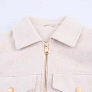 Detail view of beige zip-up jacket showing golden metal zipper and pocket stitching
