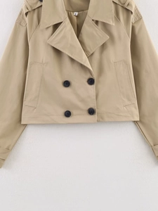 Detail of khaki cropped trench jacket featuring double-breasted buttons and shoulder epaulettes