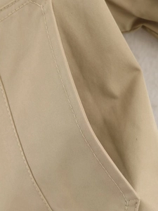 Detailed close-up of khaki double-breasted trench coat pocket with precise stitching