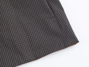 Close-up of classic grey plaid fabric detail with brown hem piping and neat stitching