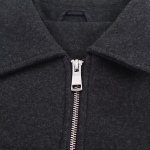 Detail of dark grey wool jacket featuring a polished silver metal zipper and stand collar