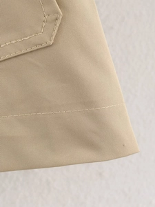 Detail of khaki cropped trench coat showing twill fabric and fine stitching on pocket
