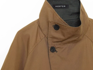 Detailed close-up of dark tan trench coat collar with green plaid lining and button