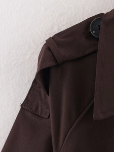 Detail view of epaulet and stitching on a dark brown double-breasted trench coat