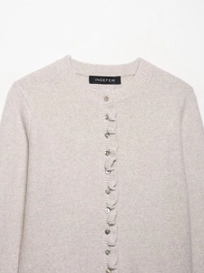 Detailed view of ruffle trim and pearl buttons on a beige knitted cardigan jacket