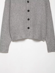 Detailed macro view of light gray knit cardigan featuring black buttons and ribbed cuffs