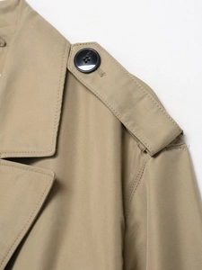 Detail shot of the khaki trench coat epaulet with a black button and twill cotton fabric