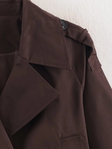 Detailed view of the double-breasted lapel and buttoned epaulets on a dark brown trench coat