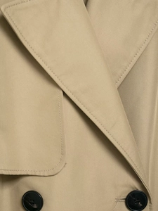 Macro shot of khaki trench coat featuring twill fabric texture and black buttons detail