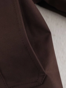Macro detail of fine twill texture and precision stitching on a brown trench coat