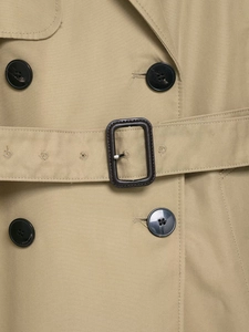 Detailed close-up of khaki trench coat featuring double-breasted buttons and belted waist