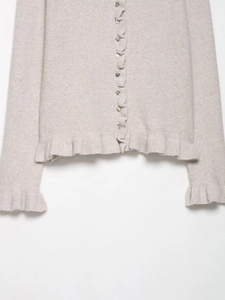Close-up of beige knit cardigan featuring delicate ruffle edges and pearl-like buttons