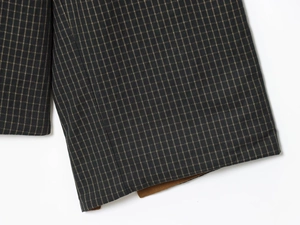 Detailed close-up of grey plaid trench coat fabric with yellow checks and brown lining