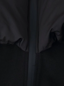 Detail of black puffer jacket showing smooth synthetic fabric and ribbed knit stitching