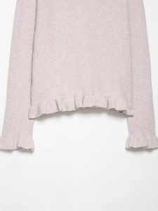 Detail of oatmeal knit cardigan showing delicate ruffle hem and soft wool texture