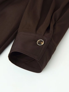 Detail of dark brown sleeve cuff with amber button and golden metal trim finish