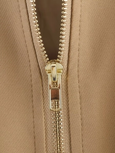 Detailed macro shot of a gold metal zipper on a khaki twill fabric jacket
