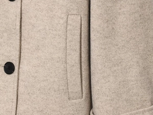 Detailaufnahme des beigen Wollmantels mit Seitentasche und schwarzem Knopf-Detail