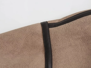 Dettaglio del tessuto scamosciato color cammello con bordo in pelle marrone e cuciture