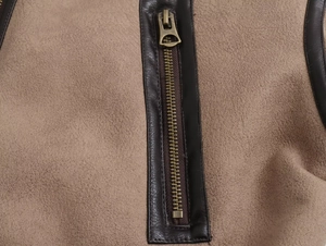 Dettaglio ravvicinato di una giacca in pelle scamosciata marrone con zip in bronzo antico