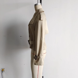 Detail of beige cropped trench coat featuring shoulder epaulettes and classic waist buckle