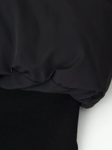 Detailed macro view of black cropped puffer jacket showing ribbed elastic hem and matte fabric