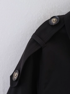 Detail shot of black trench coat shoulder with epaulette and textured horn button