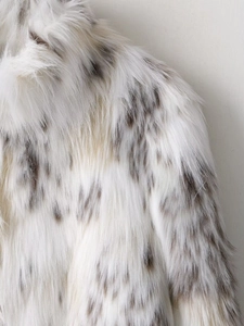 Gros plan sur un manteau en fausse fourrure blanche avec taches grises et texture douce