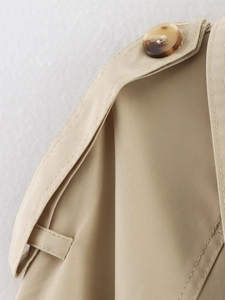 Macro detail of khaki trench coat shoulder strap with amber resin button and twill texture
