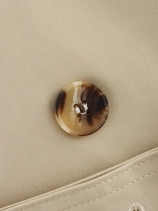 Detail shot of the faux-horn textured button and twill fabric on a khaki trench coat