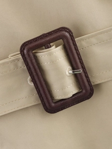 Close-up of beige trench coat waist belt featuring a brown textured buckle and metal pin