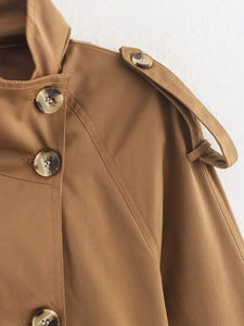 Detail of tan trench coat featuring tortoiseshell buttons and shoulder epaulettes