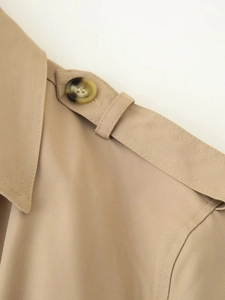 Close-up of beige trench coat epaulet detail with marble-textured button and twill fabric