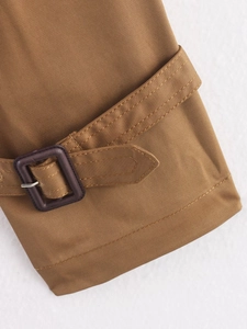 Detail of brown trench coat sleeve with a dark purple square buckle and twill fabric