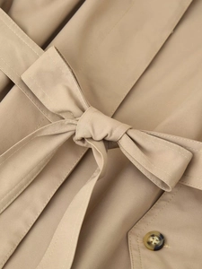 Detailed macro view of khaki trench coat fabric featuring waist belt knot and tortoise button