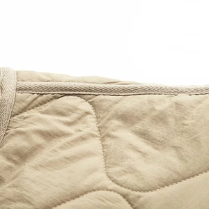 Macro detail of khaki quilted jacket fabric featuring wavy stitching and woven trim edges