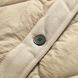 Macro detail of diamond-quilted beige jacket with herringbone tape and black button