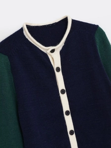 Detail of color-block knit cardigan showing navy body, green sleeves and white trim accents